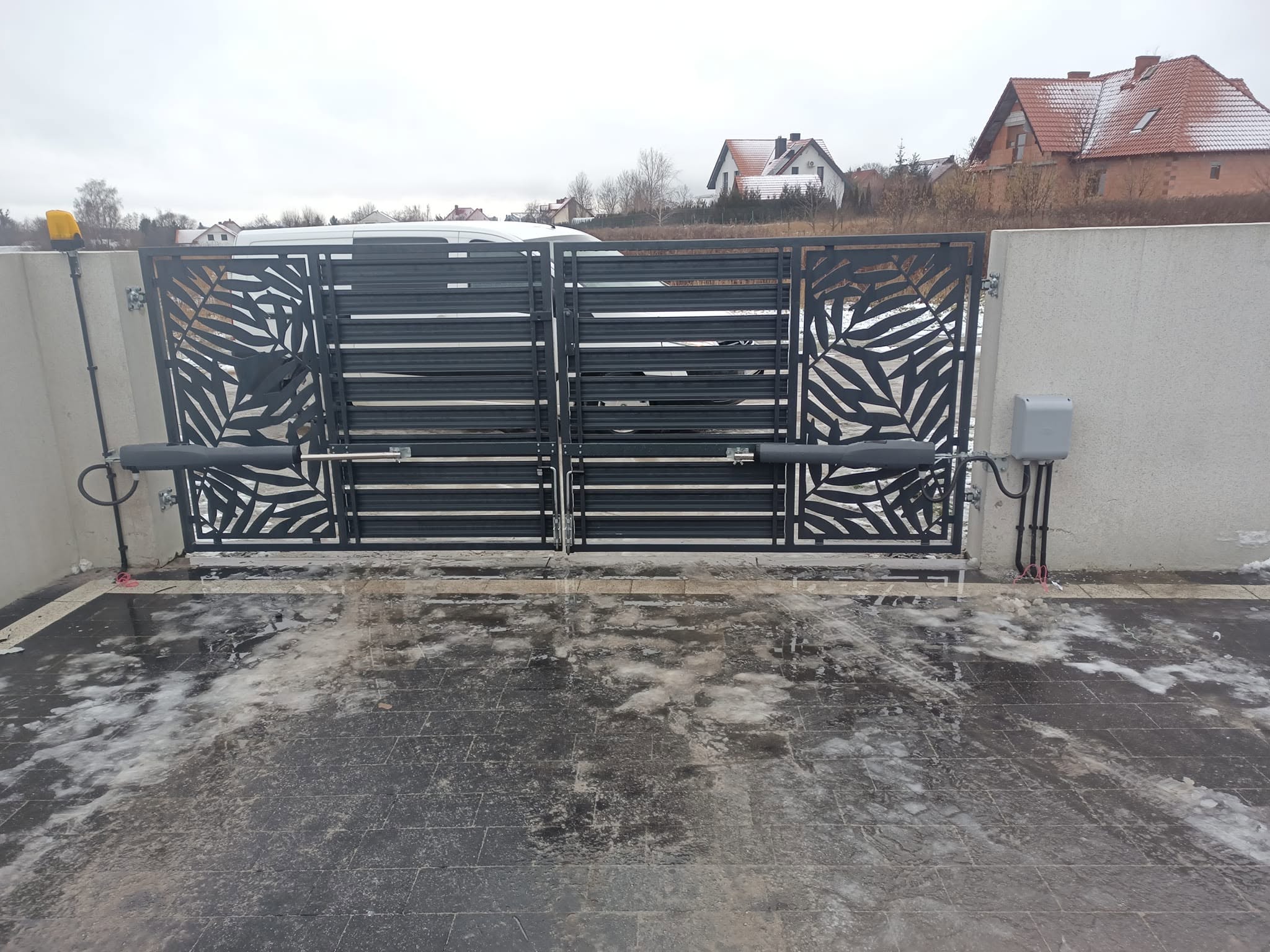 Dwuskrzydłowa brama wjazdowa z dekoracyjnym wzorem i napędami ramieniowymi
